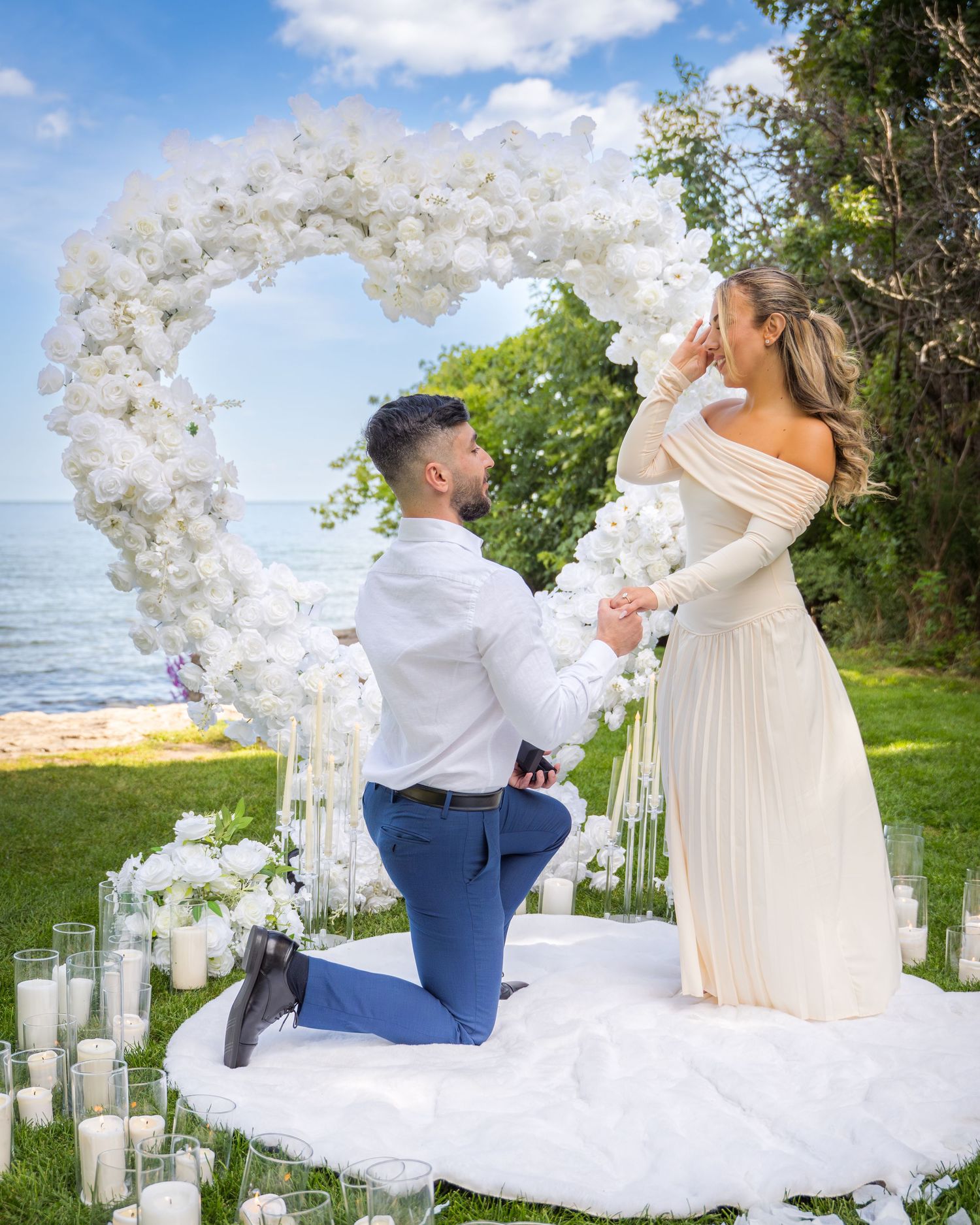 Outdoor proposal scene with white balloon arch and scattered candles in a garden setting.