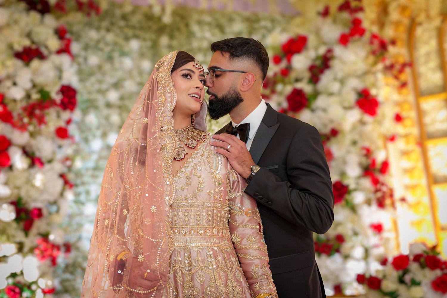 Intimate wedding moments captured against luxurious floral wall with red roses.