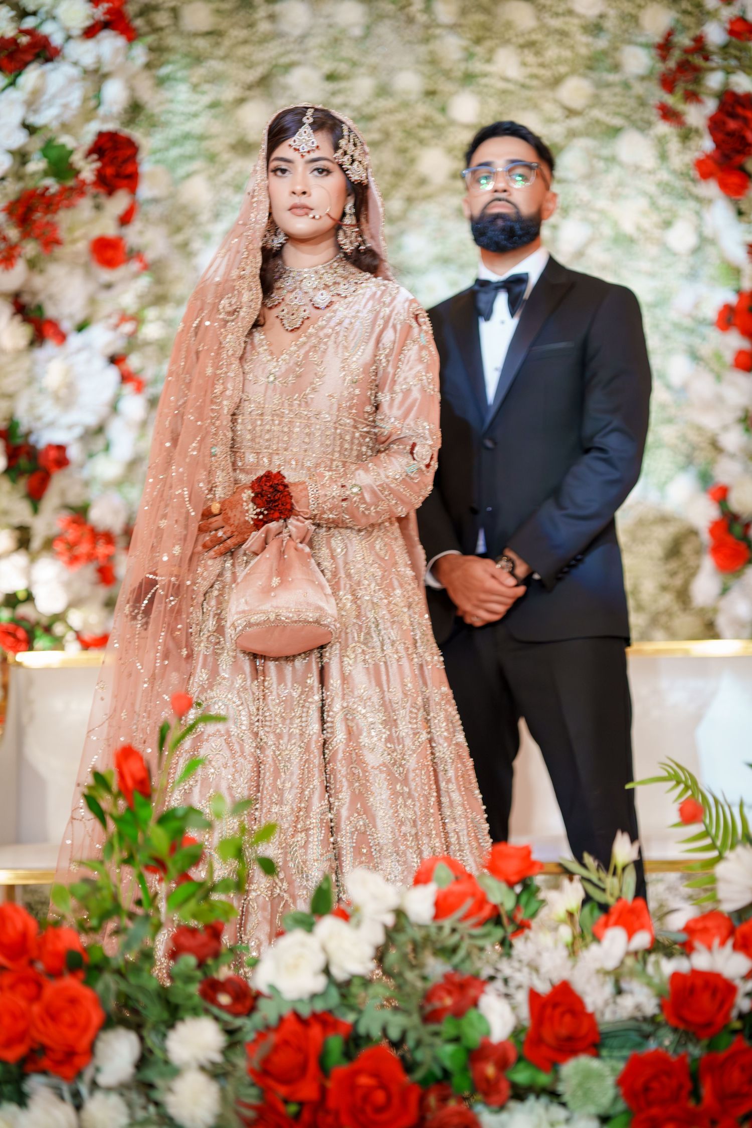 Wedding ceremony setup with red and white floral wall backdrop and traditional attire.
