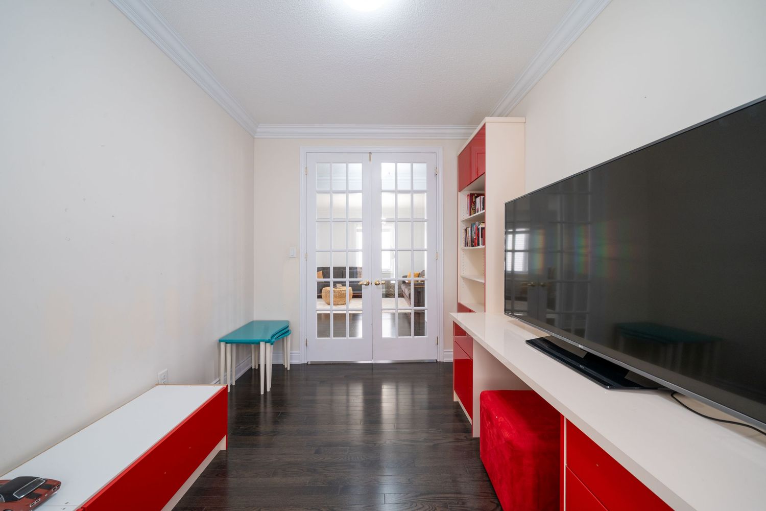 Modern room interior with red furniture, white walls, dark wood flooring and a large flat screen TV mounted on the wall.