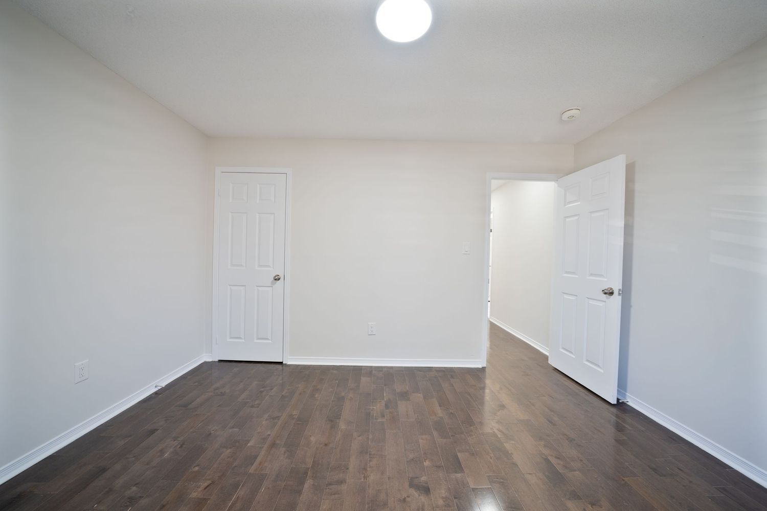Modern apartment interior with hardwood floors, white walls, and natural lighting streaming through windows.