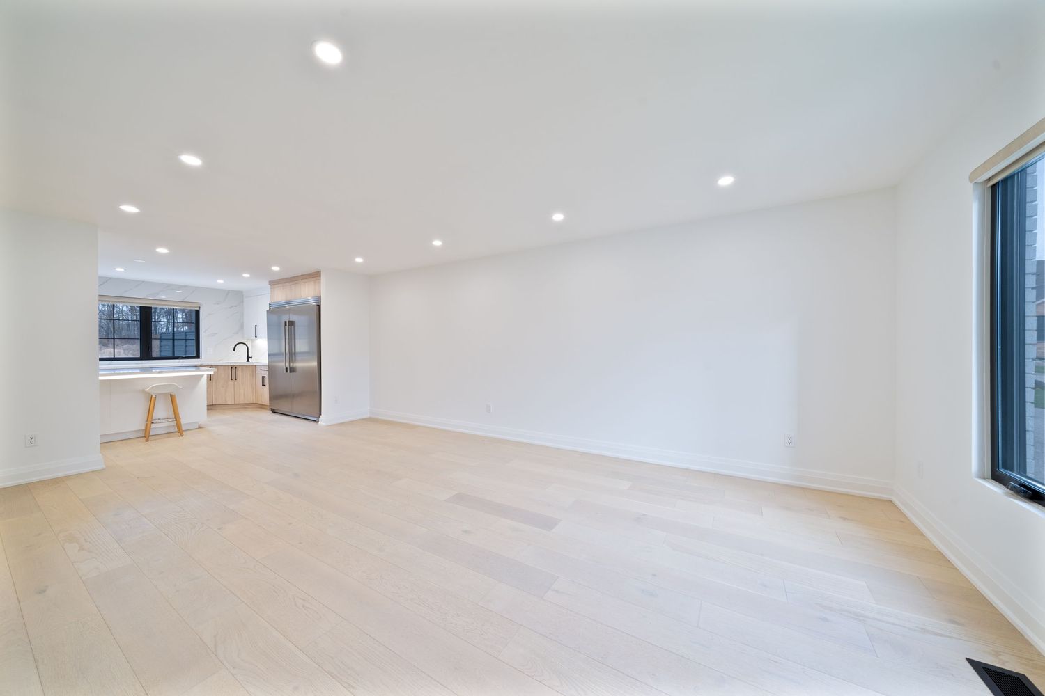 Modern minimalist white room interior with wood floors and large windows providing natural light.