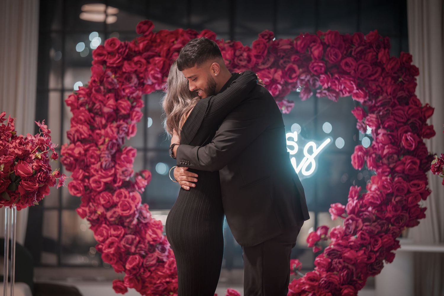 Romantic proposal scene with red rose wall and glowing neon signage.
