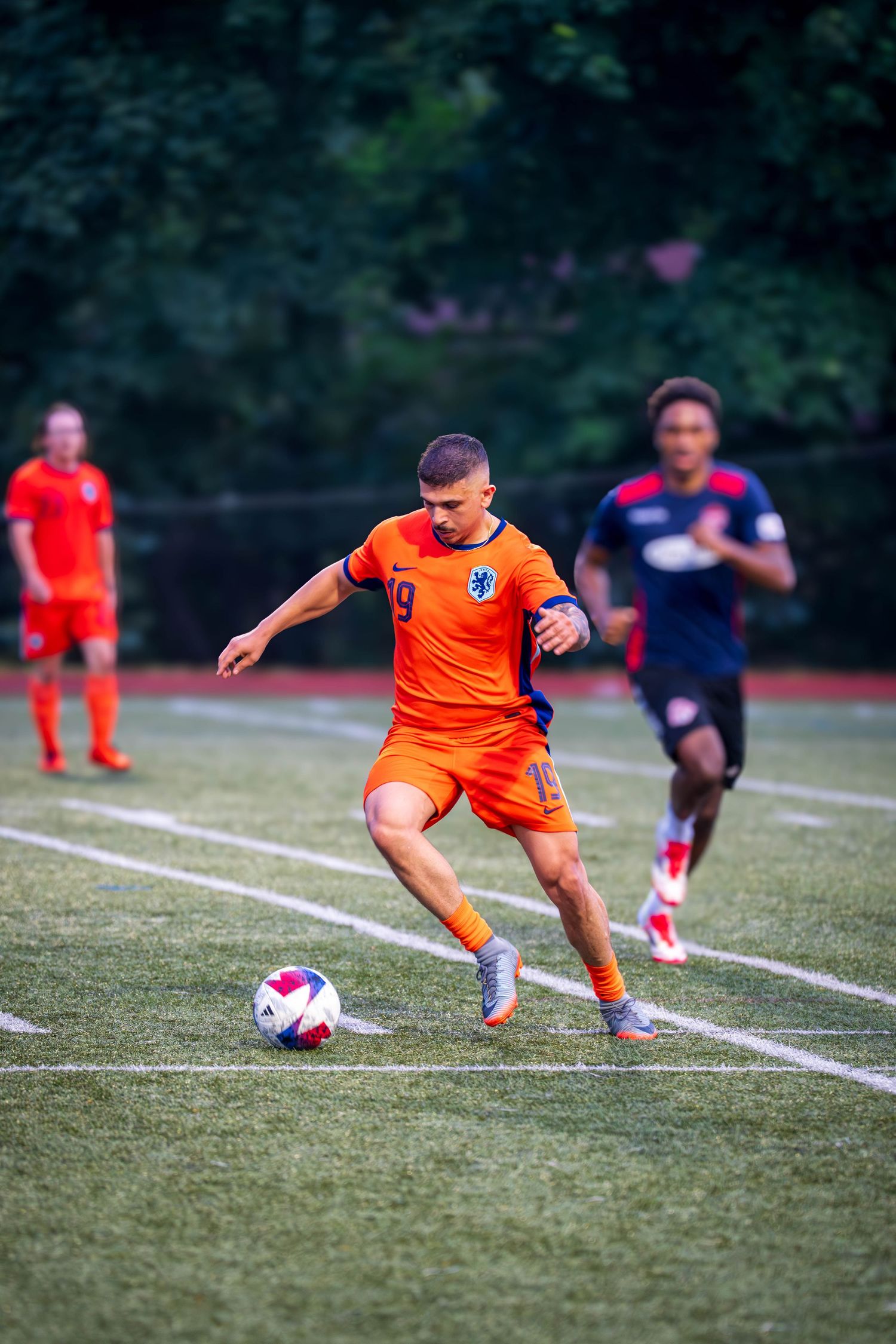 Soccer player in bright orange jersey makes contact with ball during match play.