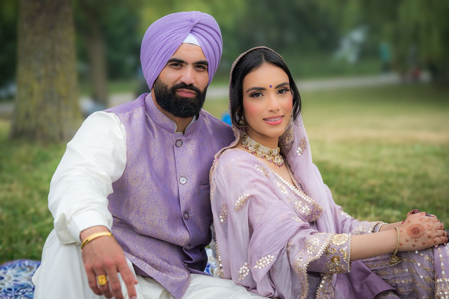 Wedding couple in purple and white traditional Sikh attire pose together on grassy lawn.