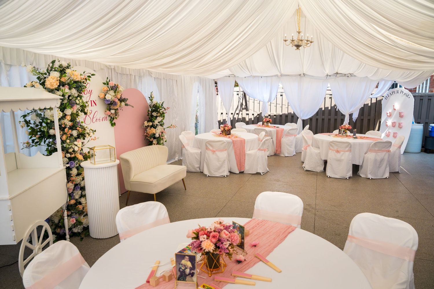 Elegant white draped wedding tent interior with pink accents and round tables.