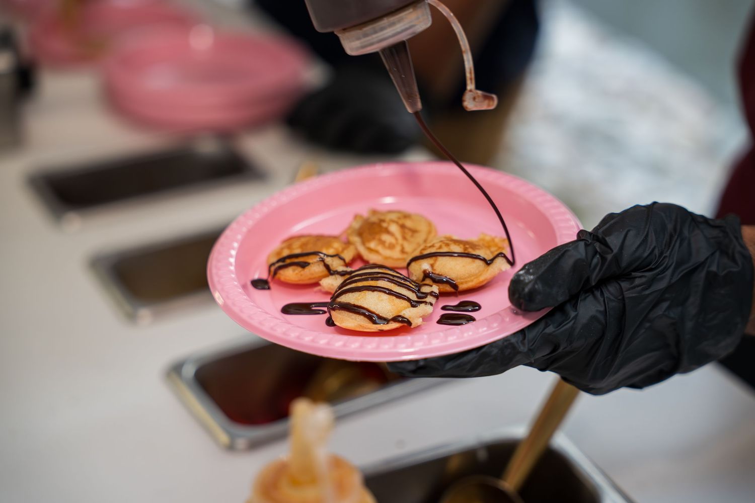 Hands in black gloves preparing dessert plates with artistic presentation.