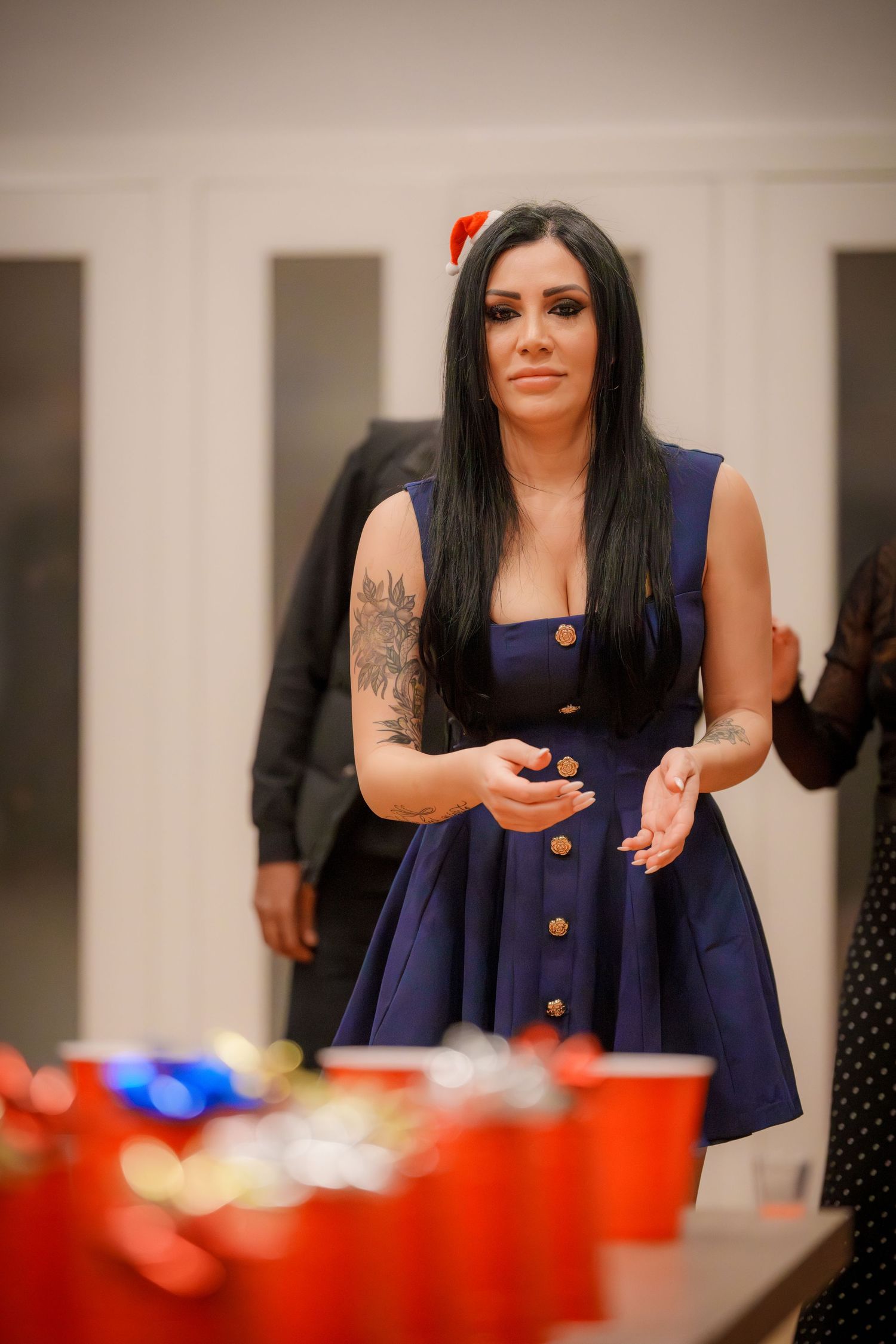 A person in a navy blue button-up dress plays a party game with red cups on a table.