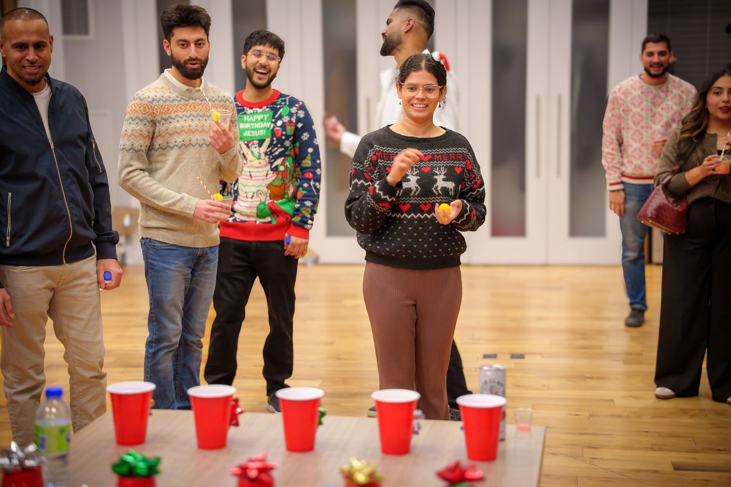Red plastic cups are lined up on tables while guests socialize in a bright indoor venue.