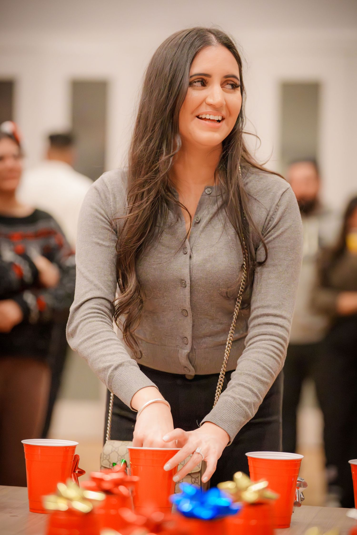 A party guest in grey attire reaches for red cups on a table with festive decorations.