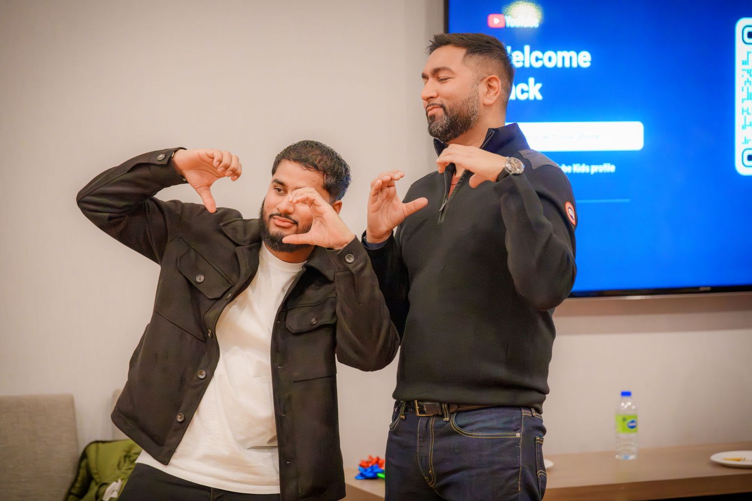 People gesturing and interacting in front of blue screen display at indoor event.