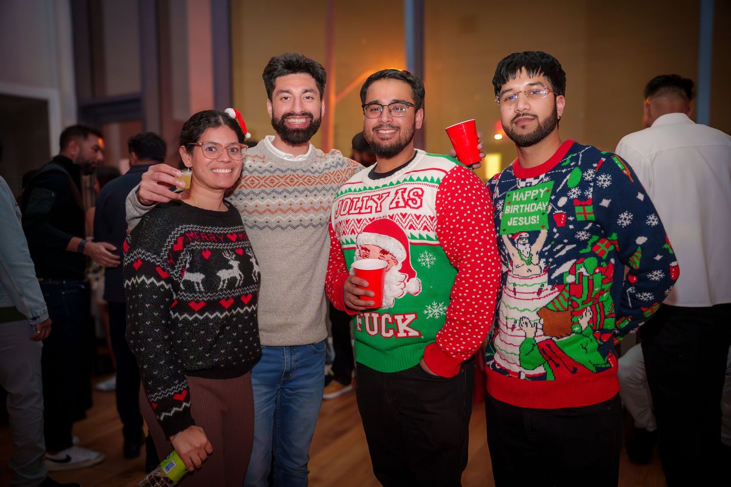 Four friends show off their festive ugly Christmas sweaters at a holiday party.