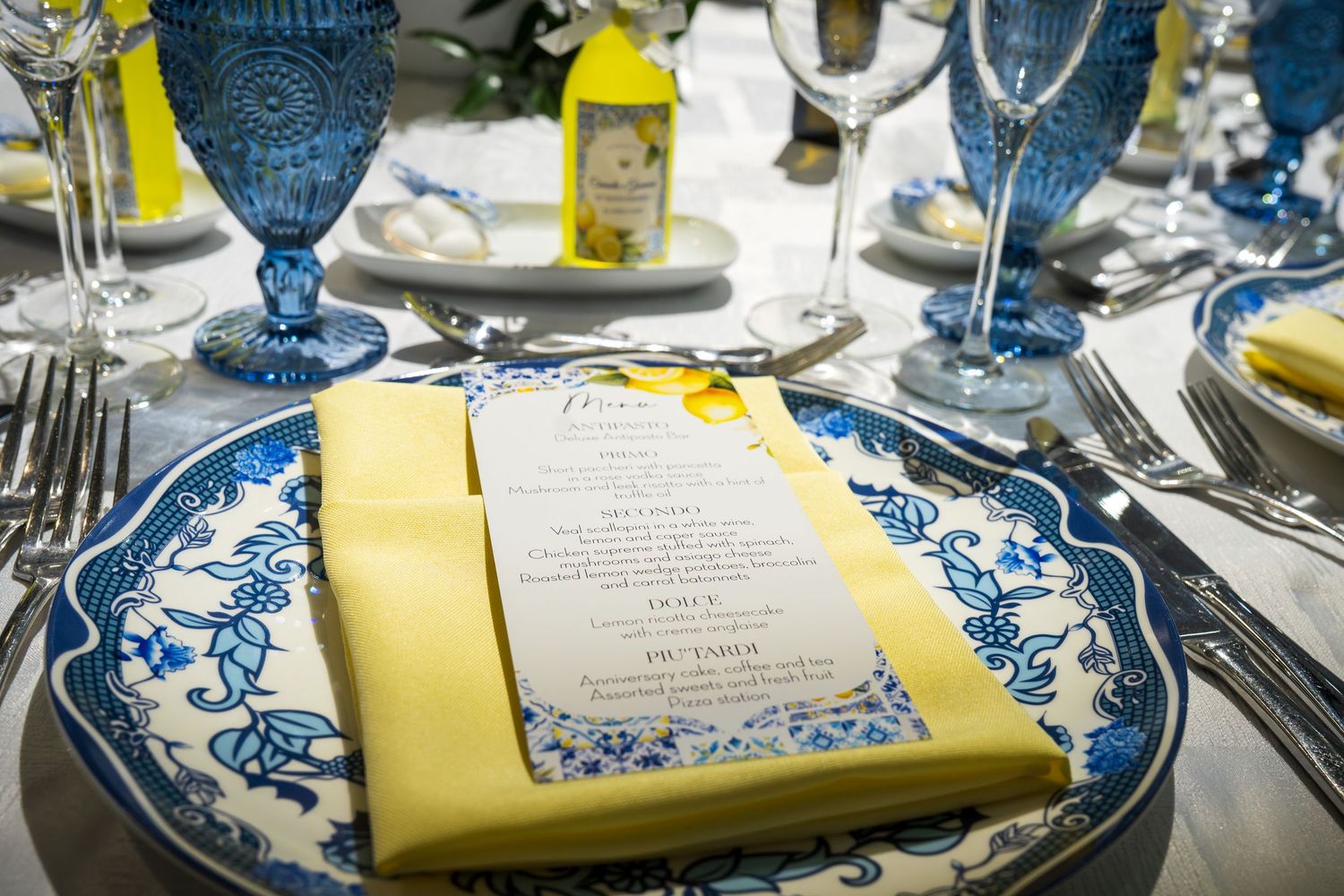 Elegant blue and white ceramic plate with yellow napkin and menu card at a formal wedding reception table setting.