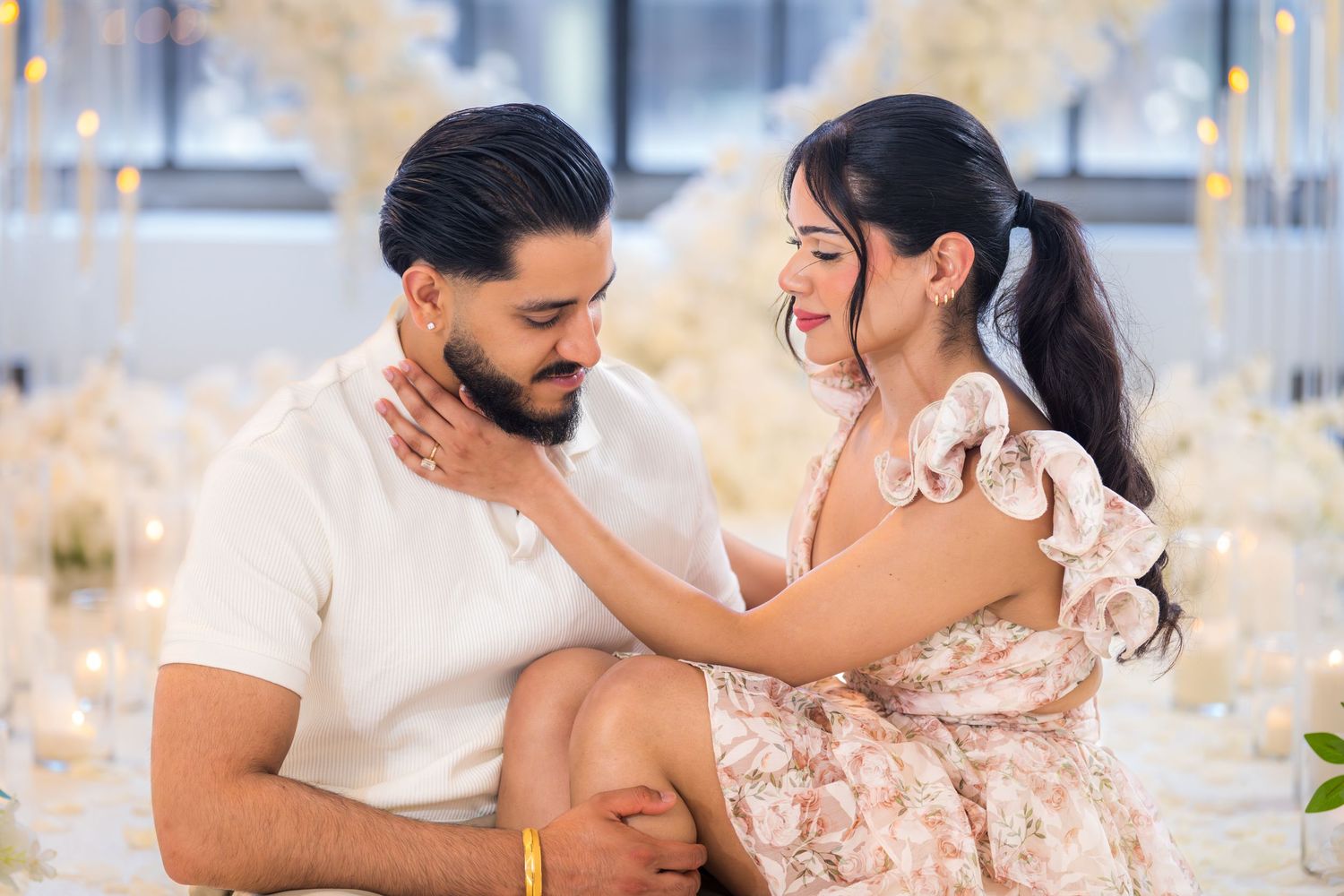 Couple sharing tender moment at romantic white floral engagement party setting.