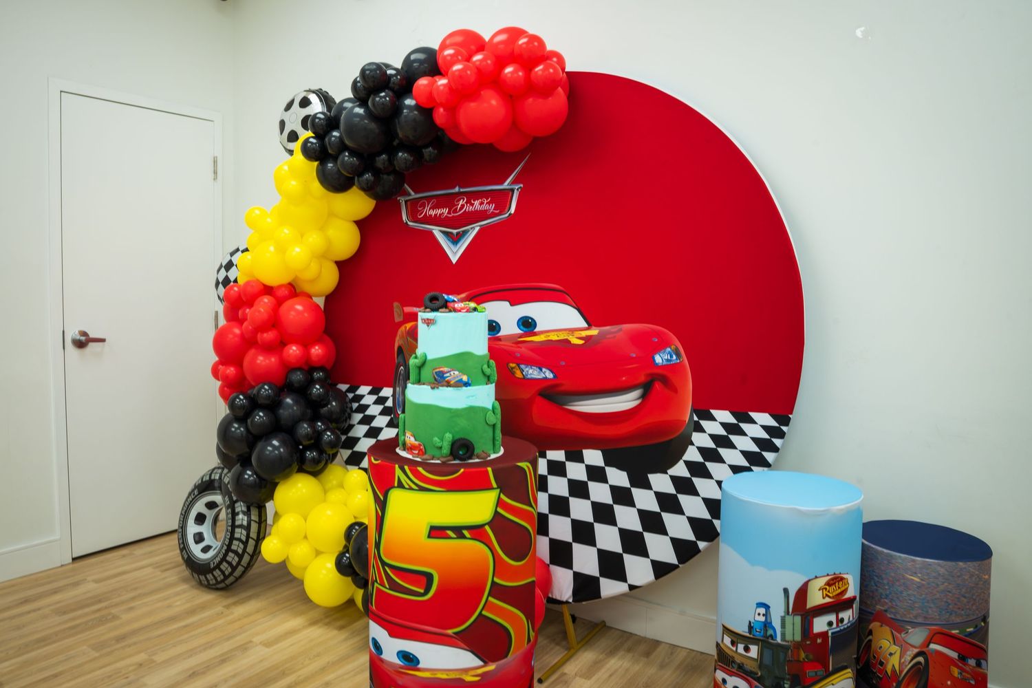Cars movie themed birthday party decoration with balloon arch, Lightning McQueen backdrop, and colorful party boxes.