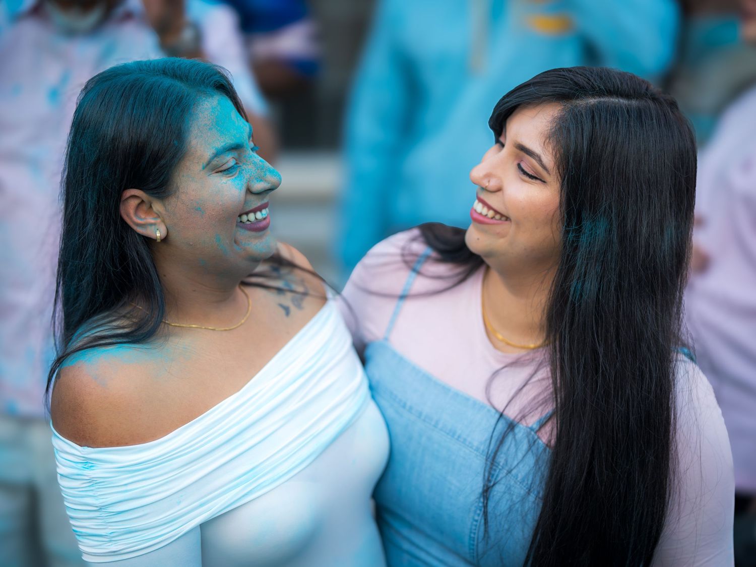 Two women laughing together with blue gender reveal powder on their faces at a celebration party.