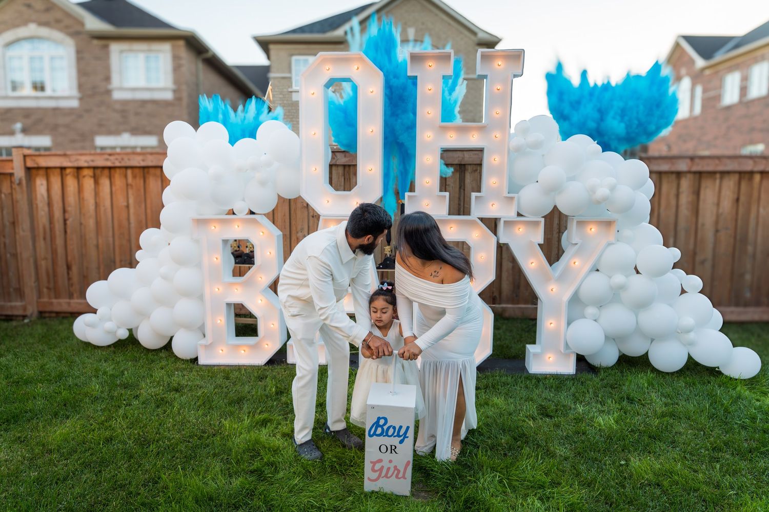 Family at gender reveal party with blue powder explosion beside OH BABY marquee letters and Boy or Girl sign.