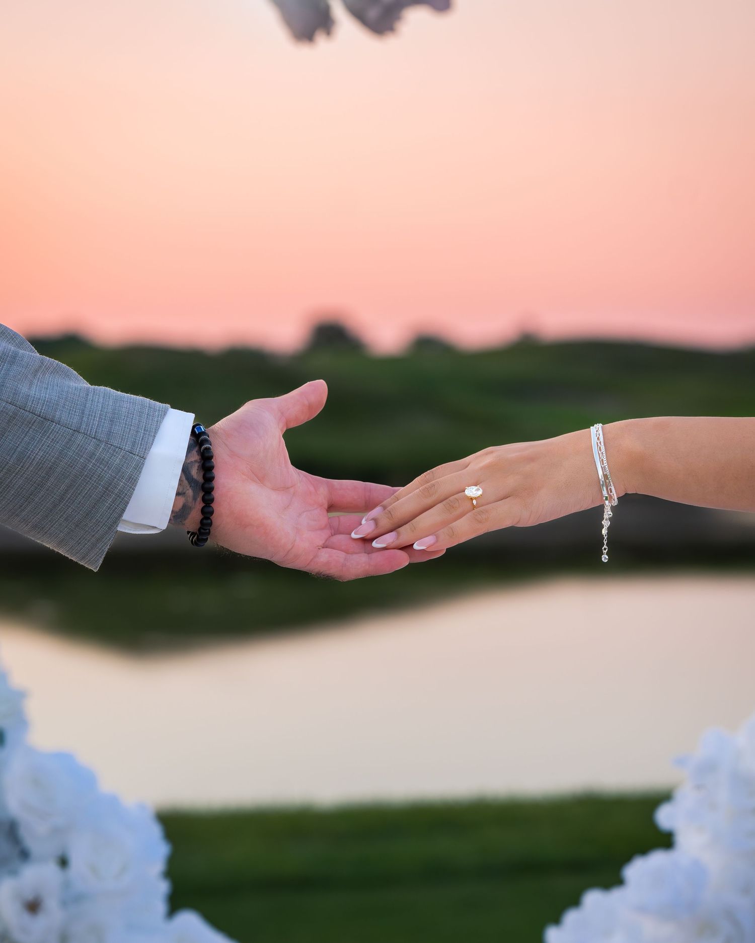 Hands reaching out against pink sunset sky with white decorations.