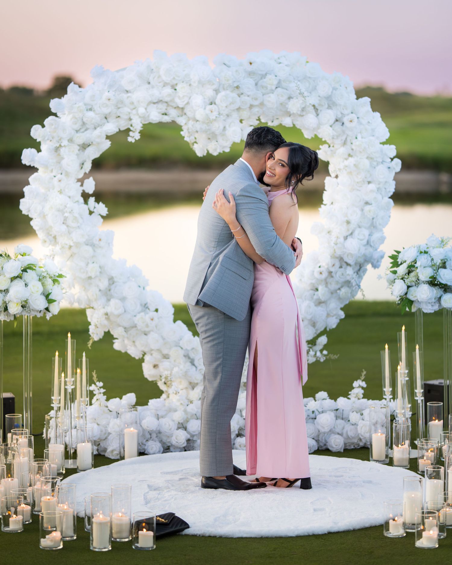 Elegant outdoor proposal scene with white orchid arch and scattered candles creating a romantic atmosphere.