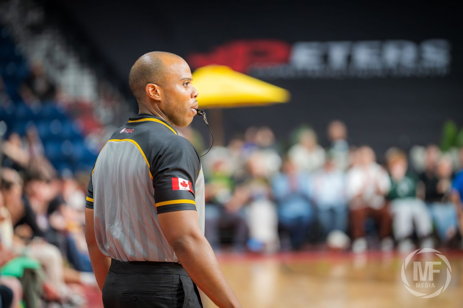 Basketball referee with whistle in mouth wearing black and gold uniform during a CEBL game.
