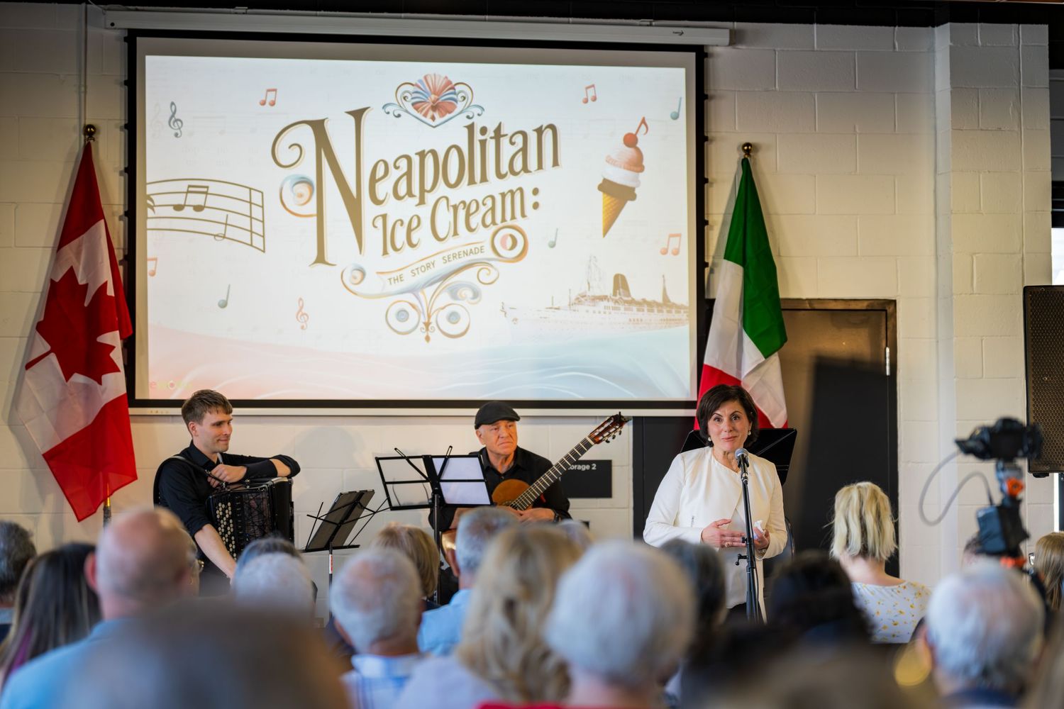 Three musicians perform on stage at a Neapolitan Ice Cream musical event with Canadian and Italian flags displayed.