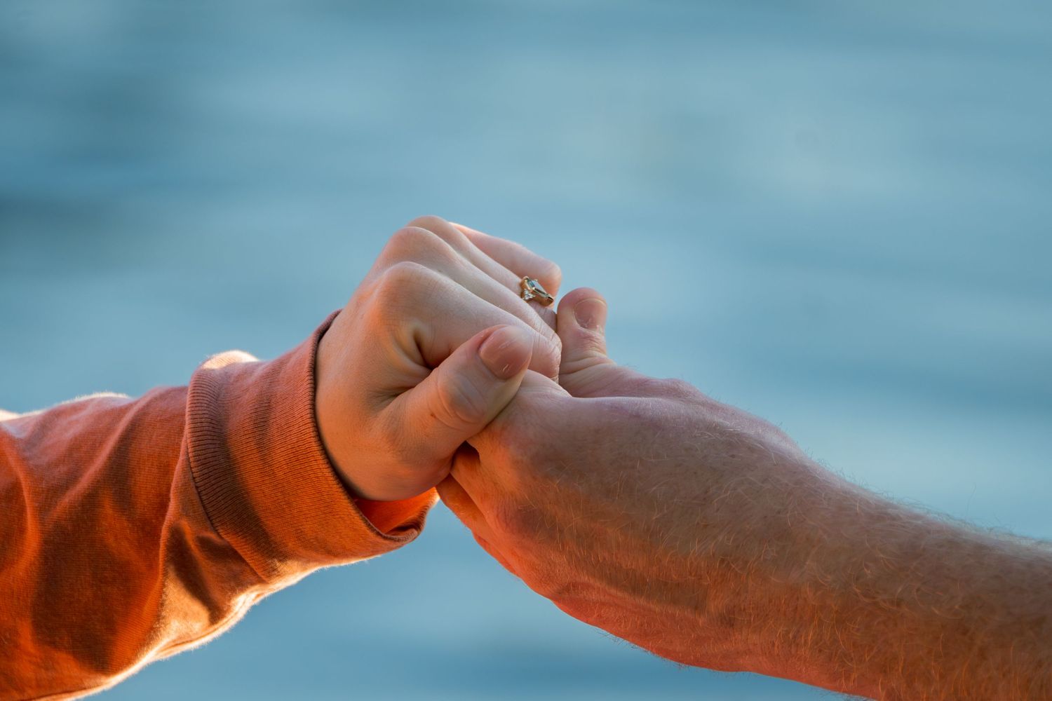 Close-up of a child and adult holding hands together near blue water, symbolizing family bond and connection.