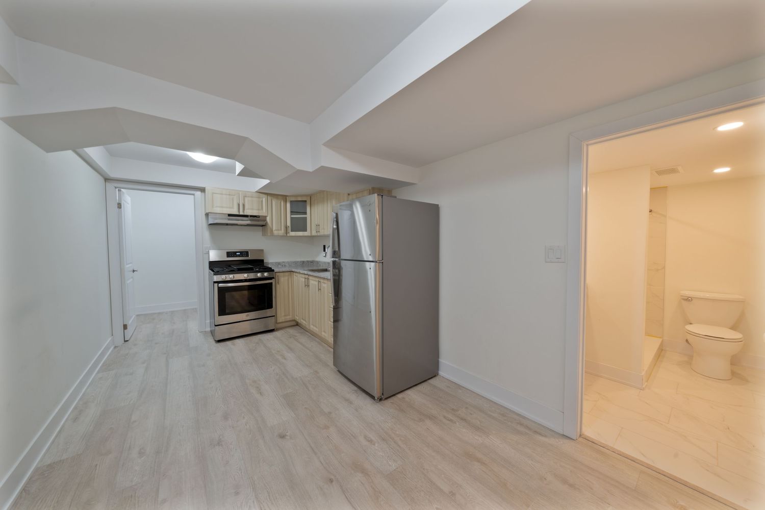 Modern white basement hallway with recessed lighting and light wood flooring leading to multiple doorways.