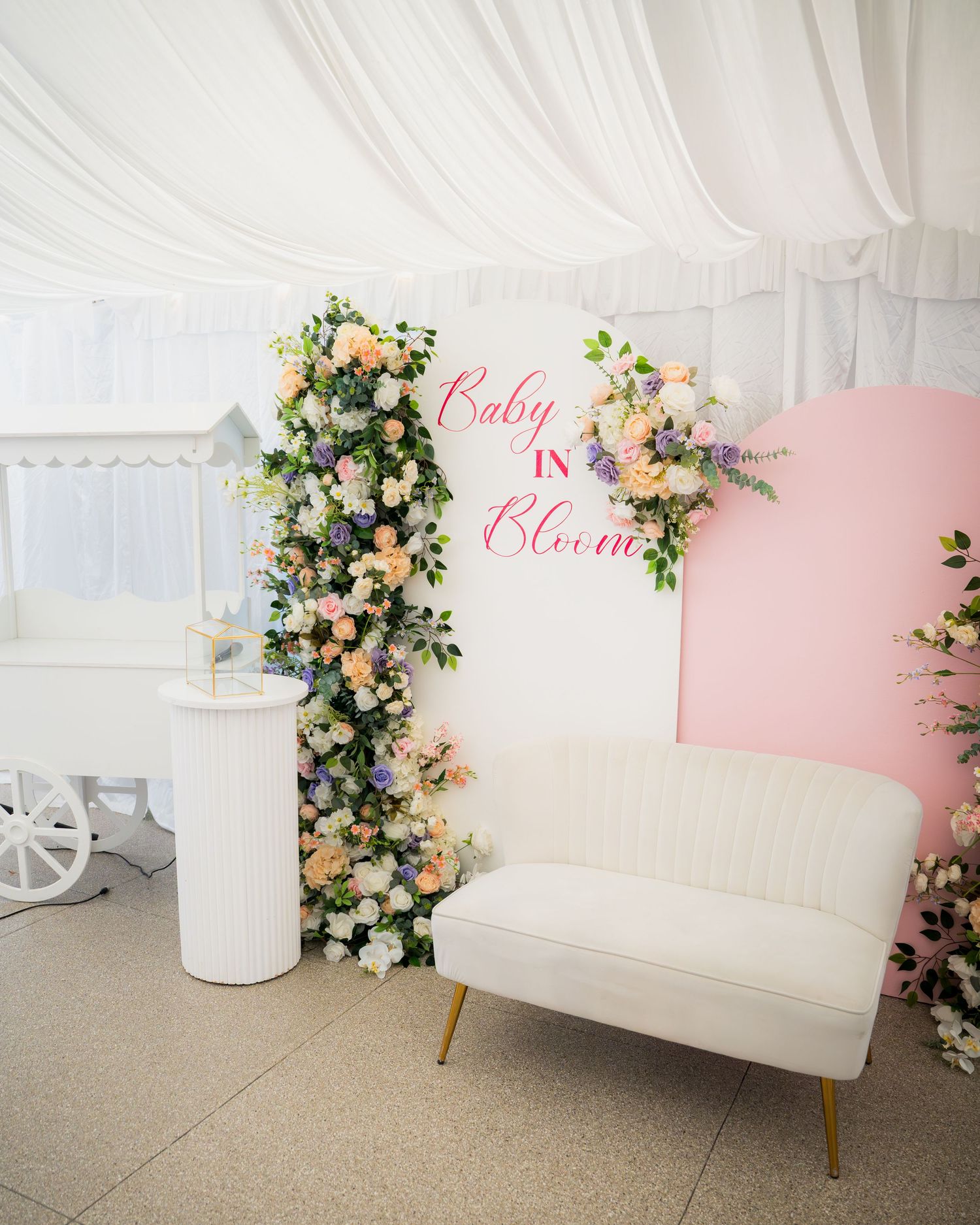 White vintage sofa against floral decorated backdrop at a baby shower celebration.
