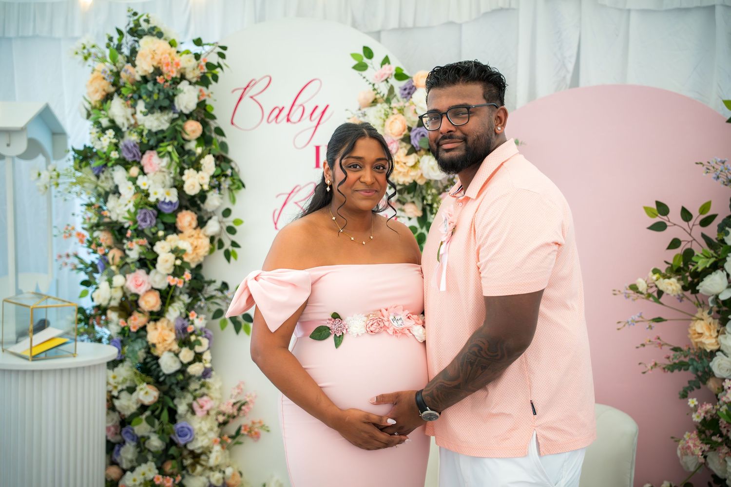 Baby shower celebration setup with elegant floral arrangements and pink backdrop.