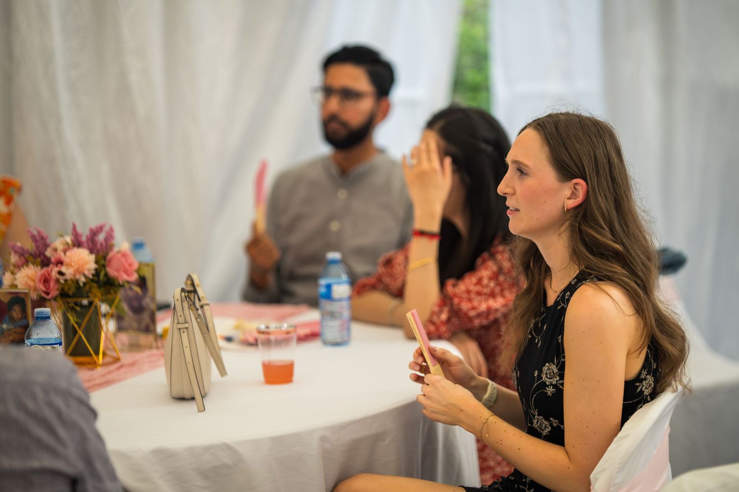 Guests engaged in conversation at a white-clothed table with floral centerpieces.