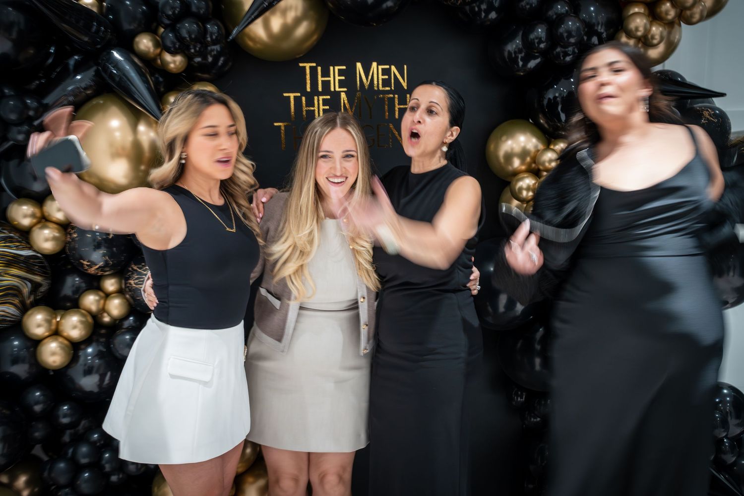Party scene with festive black and gold balloon arrangements in the background.