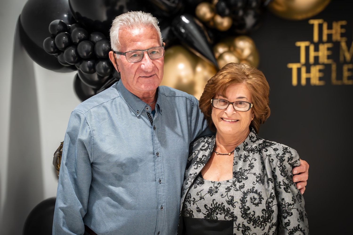 Couple posing together at formal event with gold decor and black backdrop.