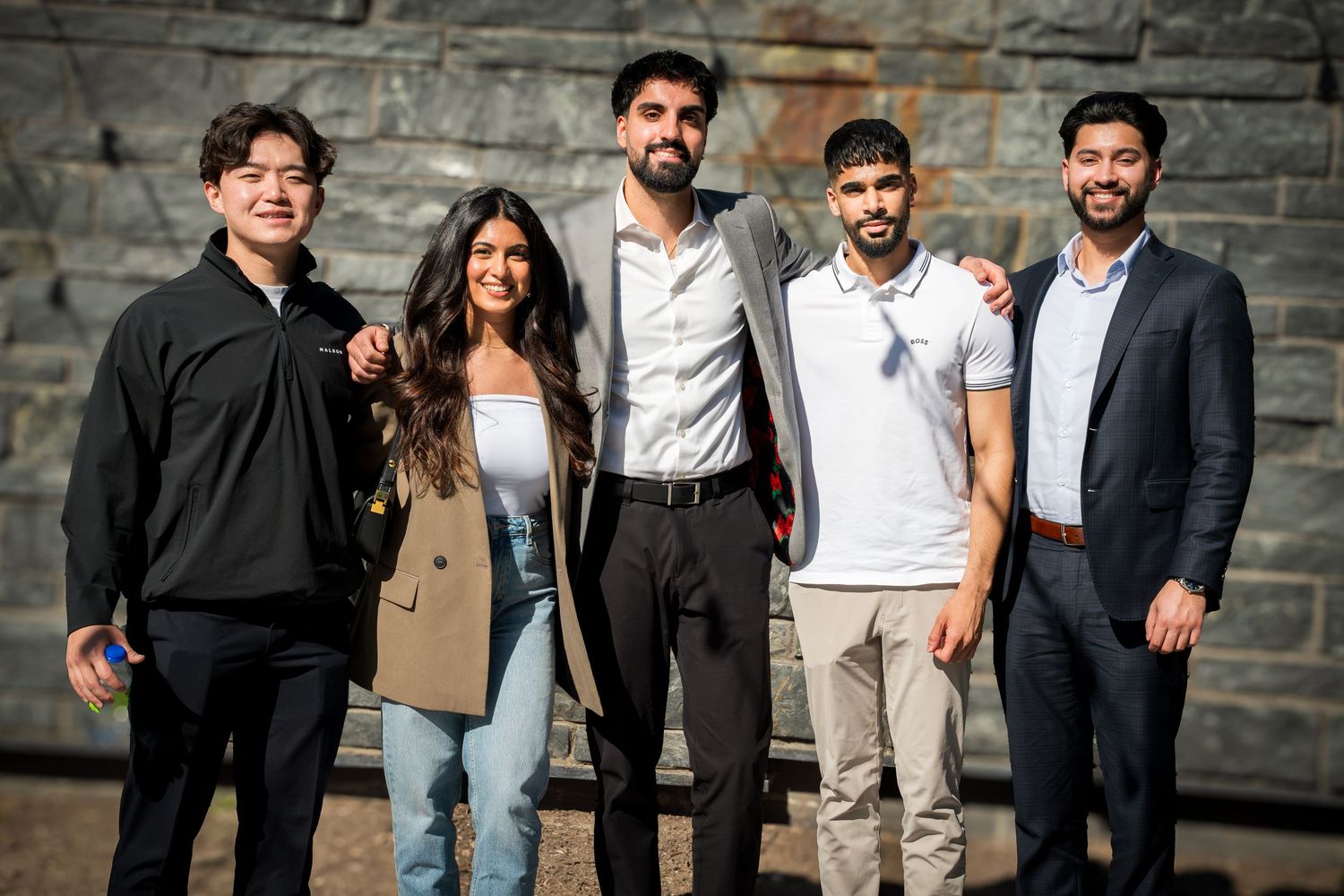 Group portrait of speakers posing against stone wall exterior.