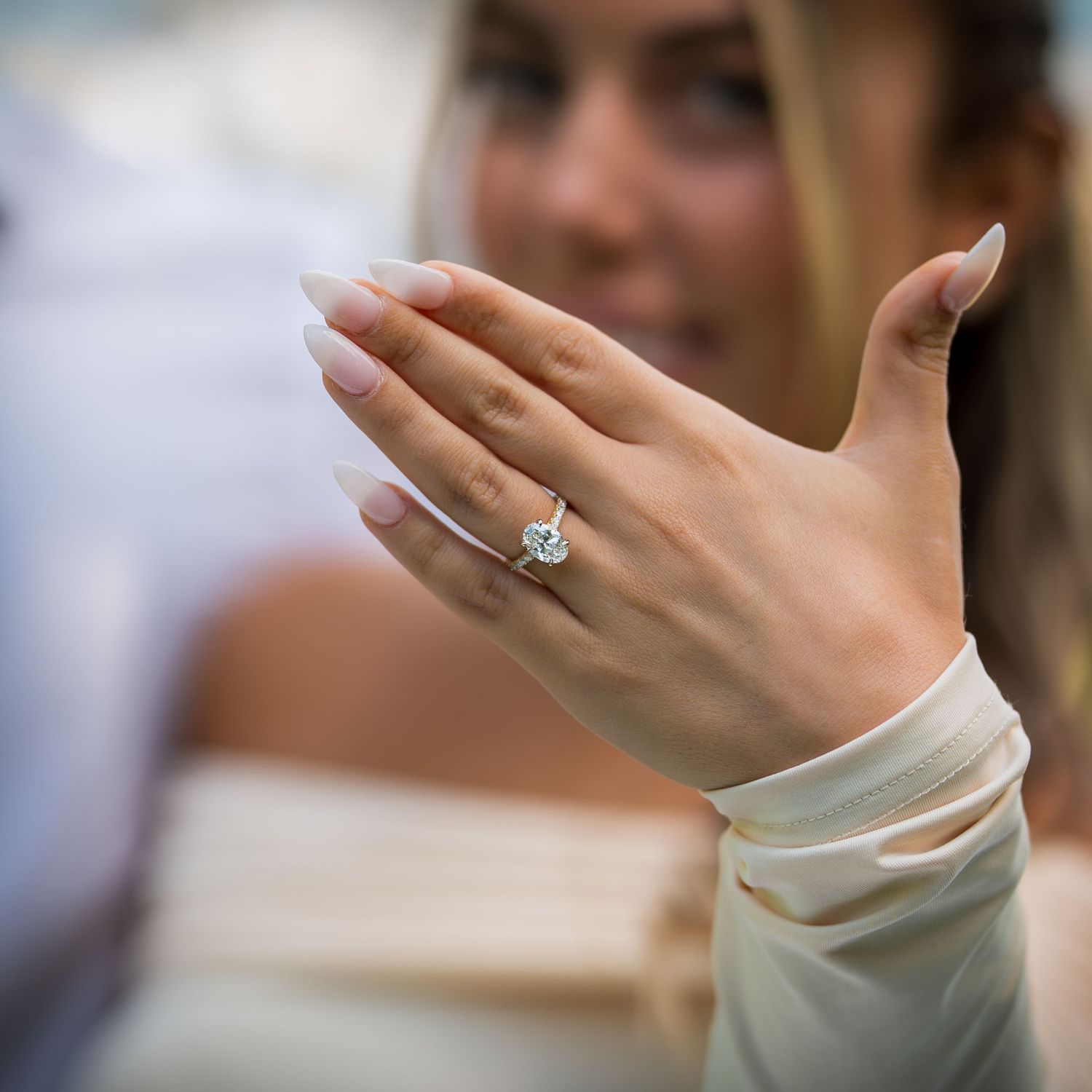 Close-up shot of a sparkling engagement ring on a hand with long-sleeved white dress.