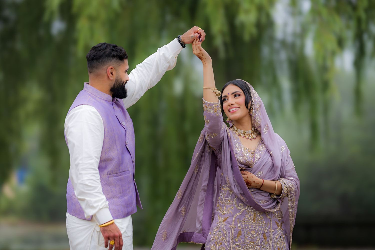 A romantic couple in matching lavender outfits share a playful moment under weeping willows.