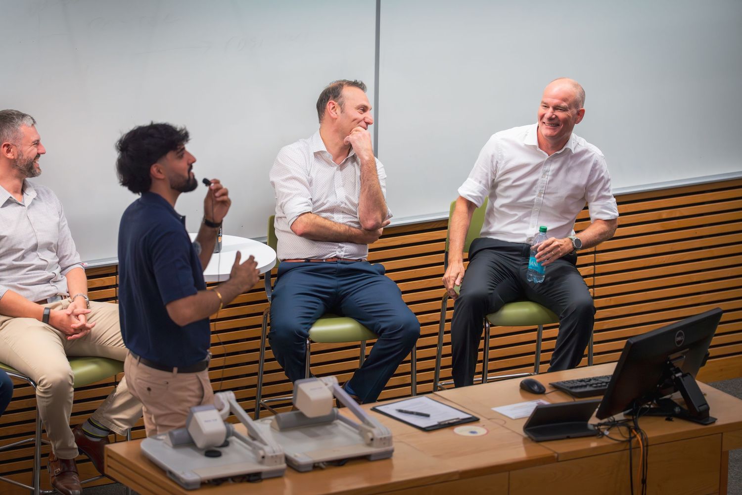 Panel of speakers engaged in discussion while seated on wooden benches.