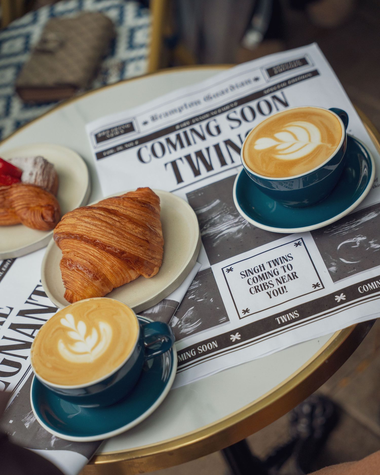 Artfully presented coffee and croissants on plates with a newspaper.