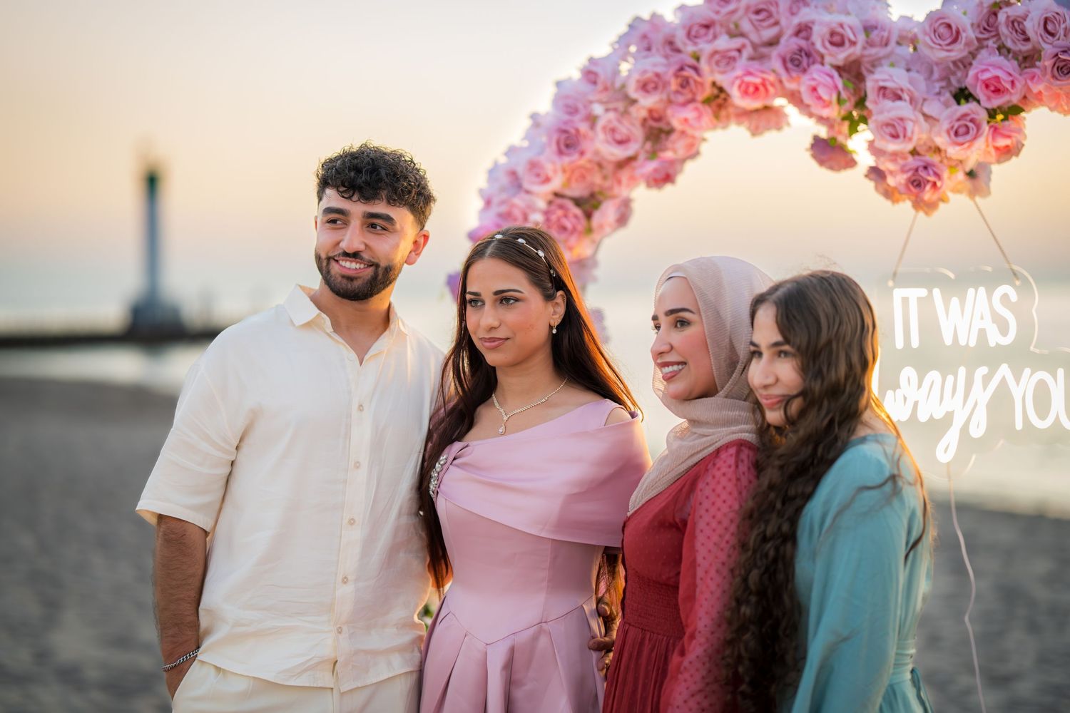 Beachside proposal celebration with family members and pink floral decorations at sunset.