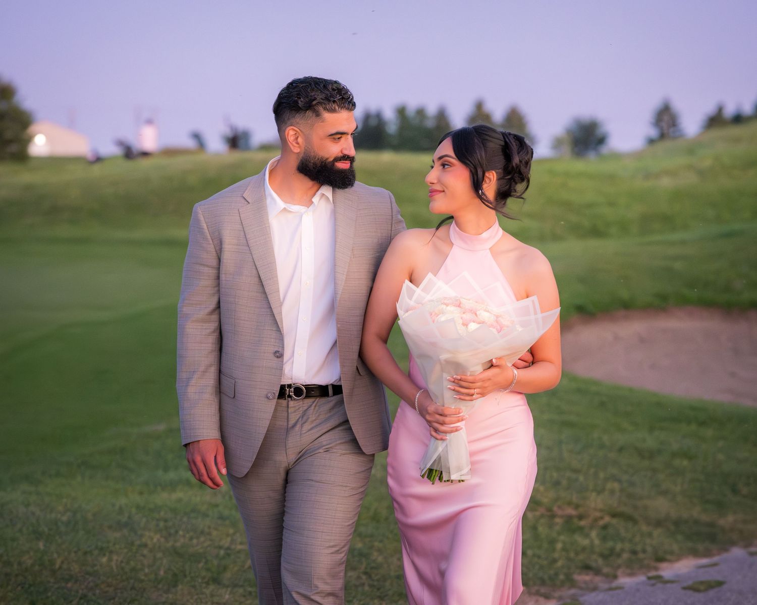 A couple walks together on a path during golden hour in coordinated formal attire.