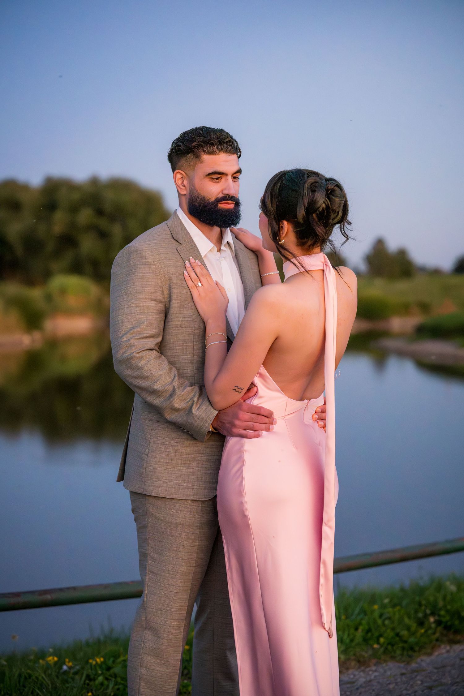 Tender moment captured between couple in formal attire against serene lake backdrop.