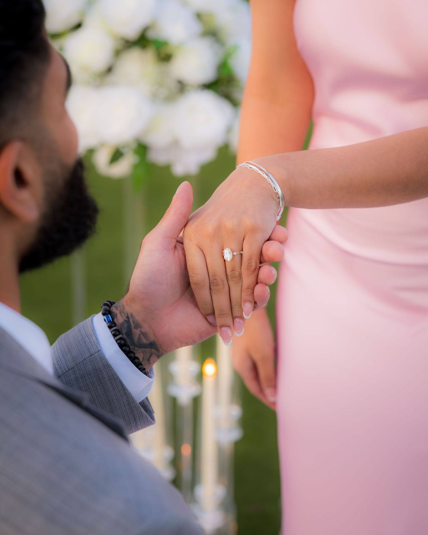 Close-up of hands showing an engagement ring against a pink dress during a sunset proposal.