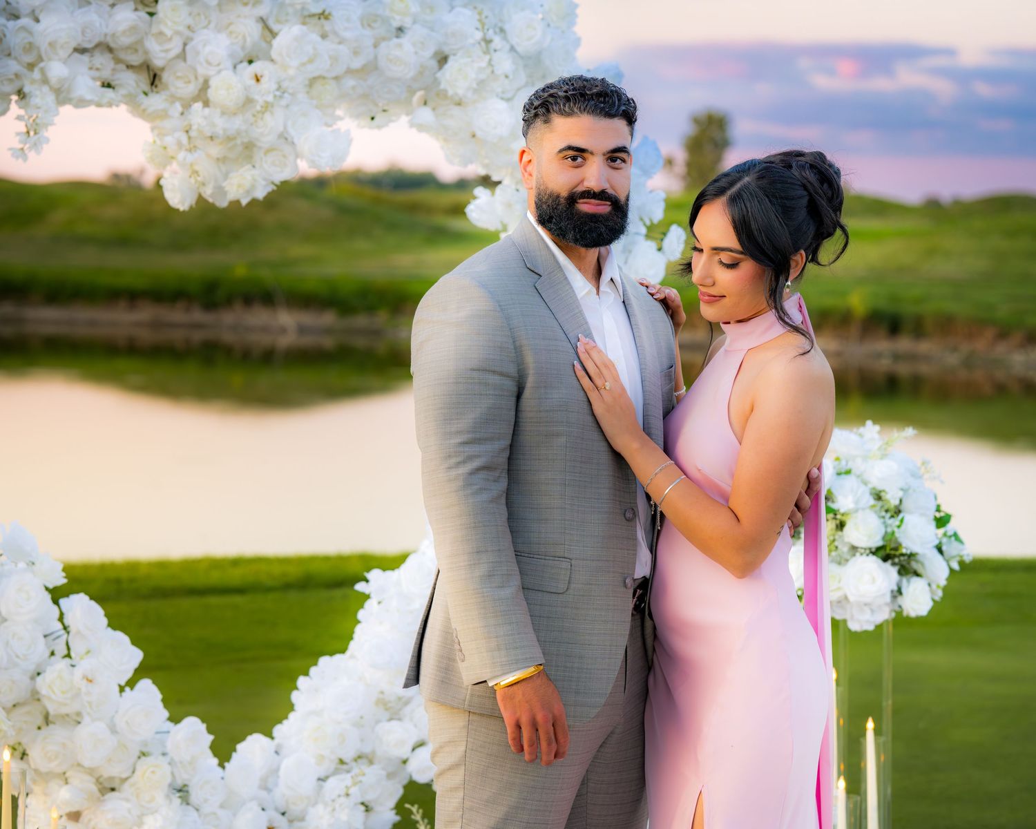A tender moment between a couple against a sunset backdrop with white floral arrangements.