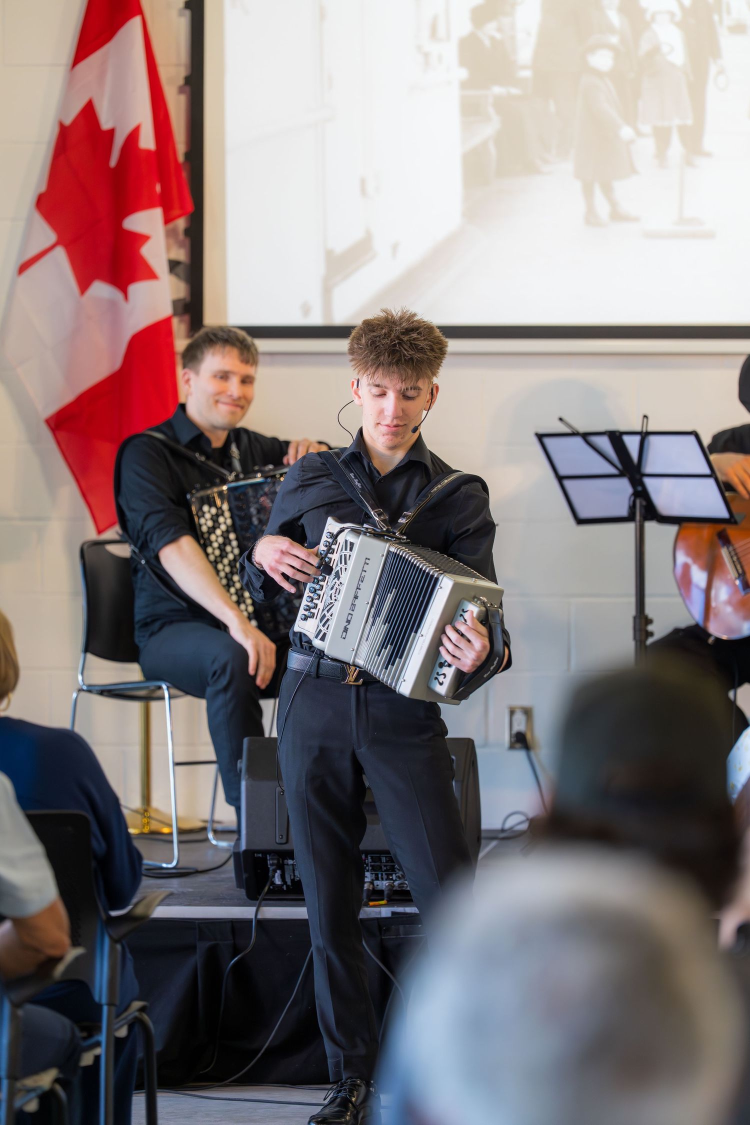 Young musician plays accordion on stage near Canadian flag at Neapolitan Ice Cream musical performance.