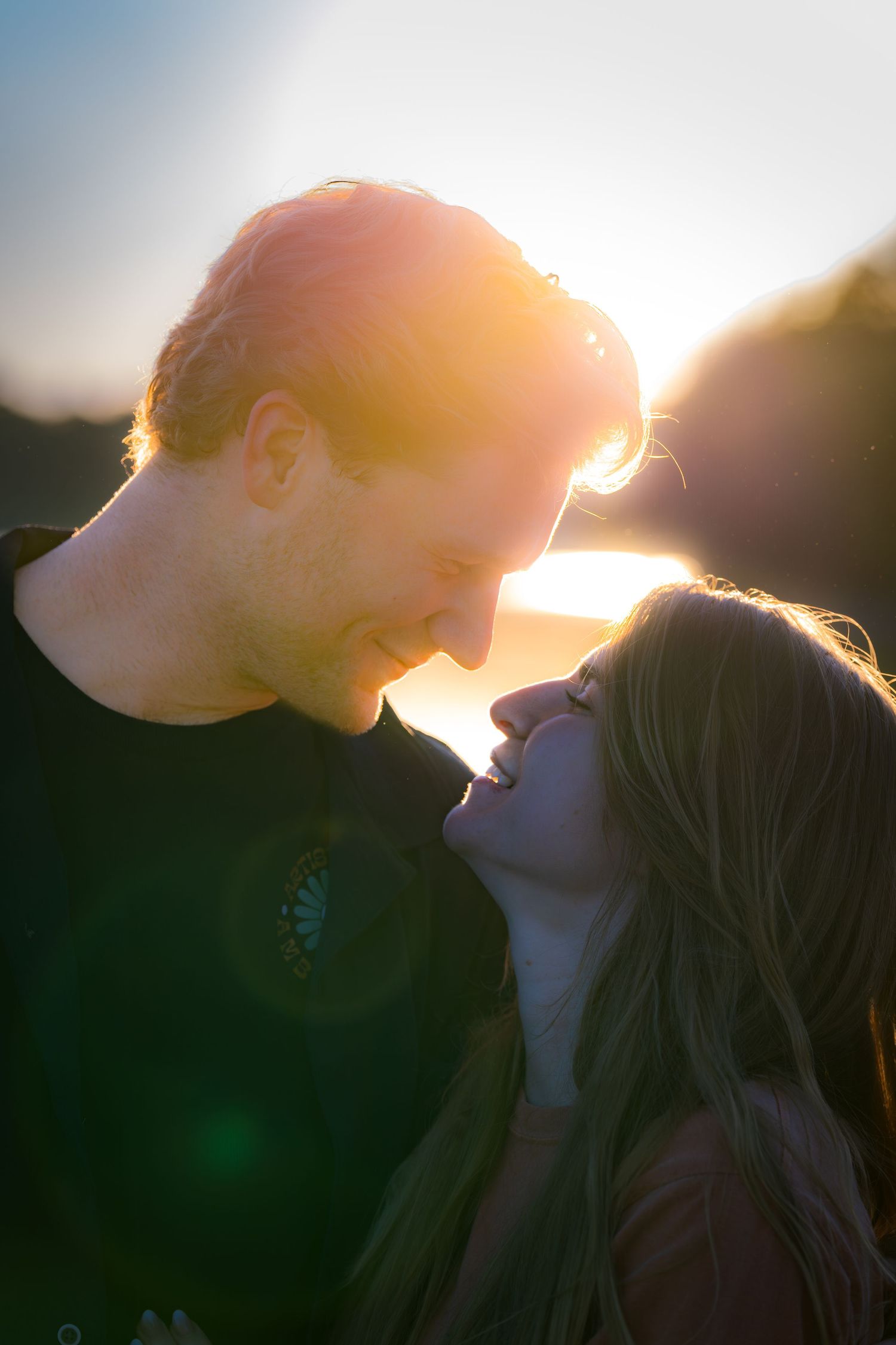 Romantic couple sharing a tender moment at golden hour sunset, bathed in warm glowing backlight.