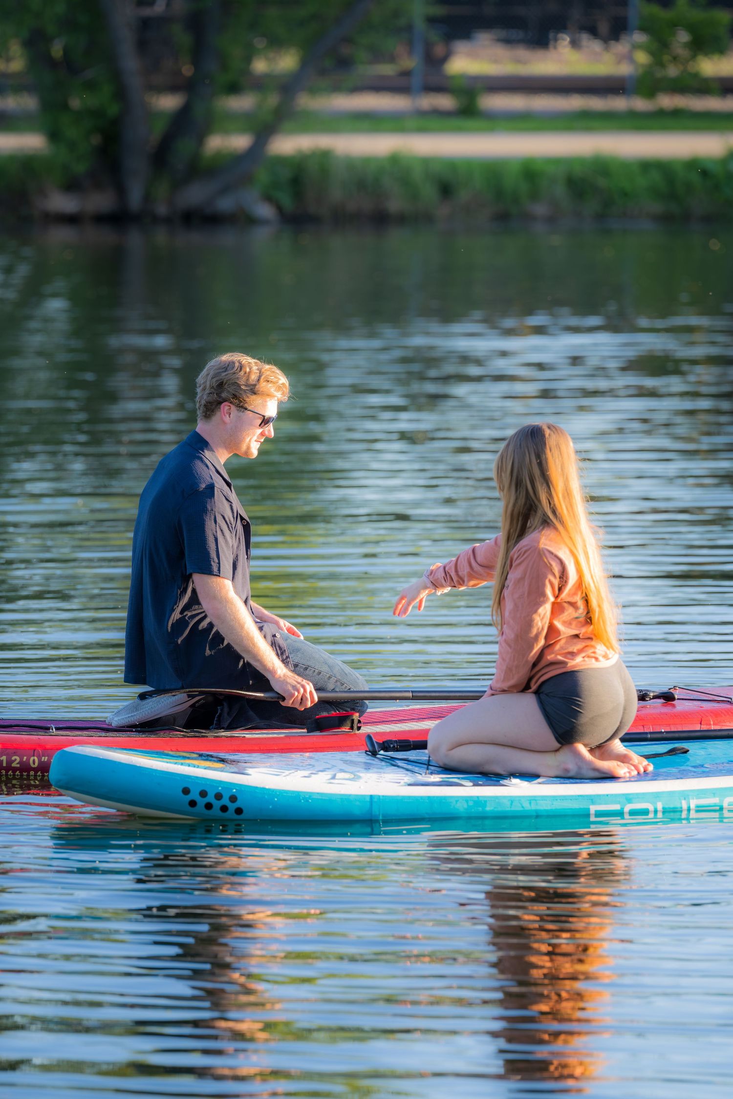 Young couple sitting face to face on a paddleboard on a calm lake during a warm sunset evening.
