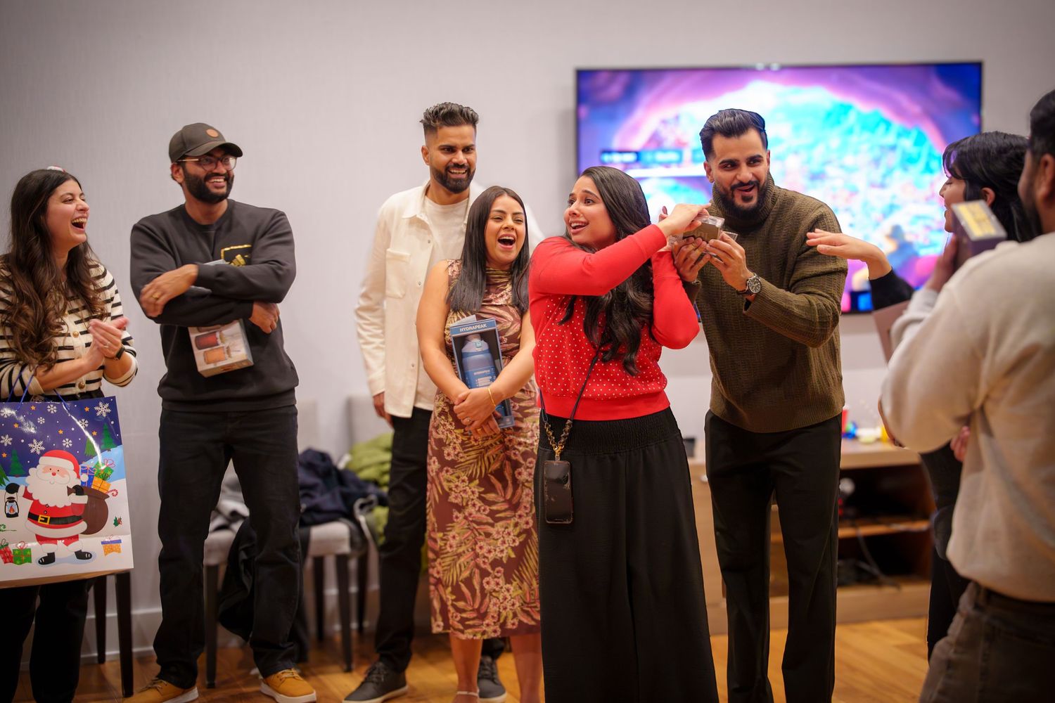 A group of party guests interact and laugh during an indoor holiday celebration.
