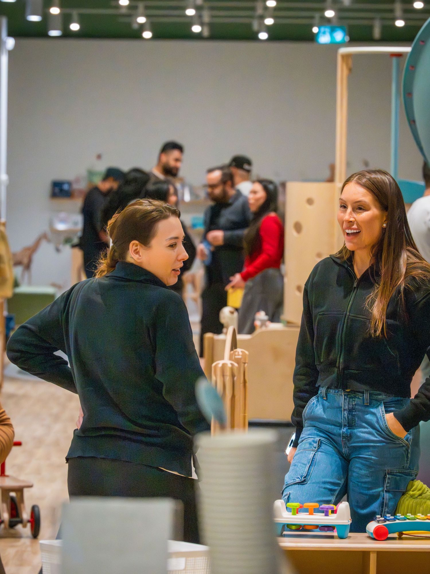 Two women in black hoodies conversing in a busy indoor play space.