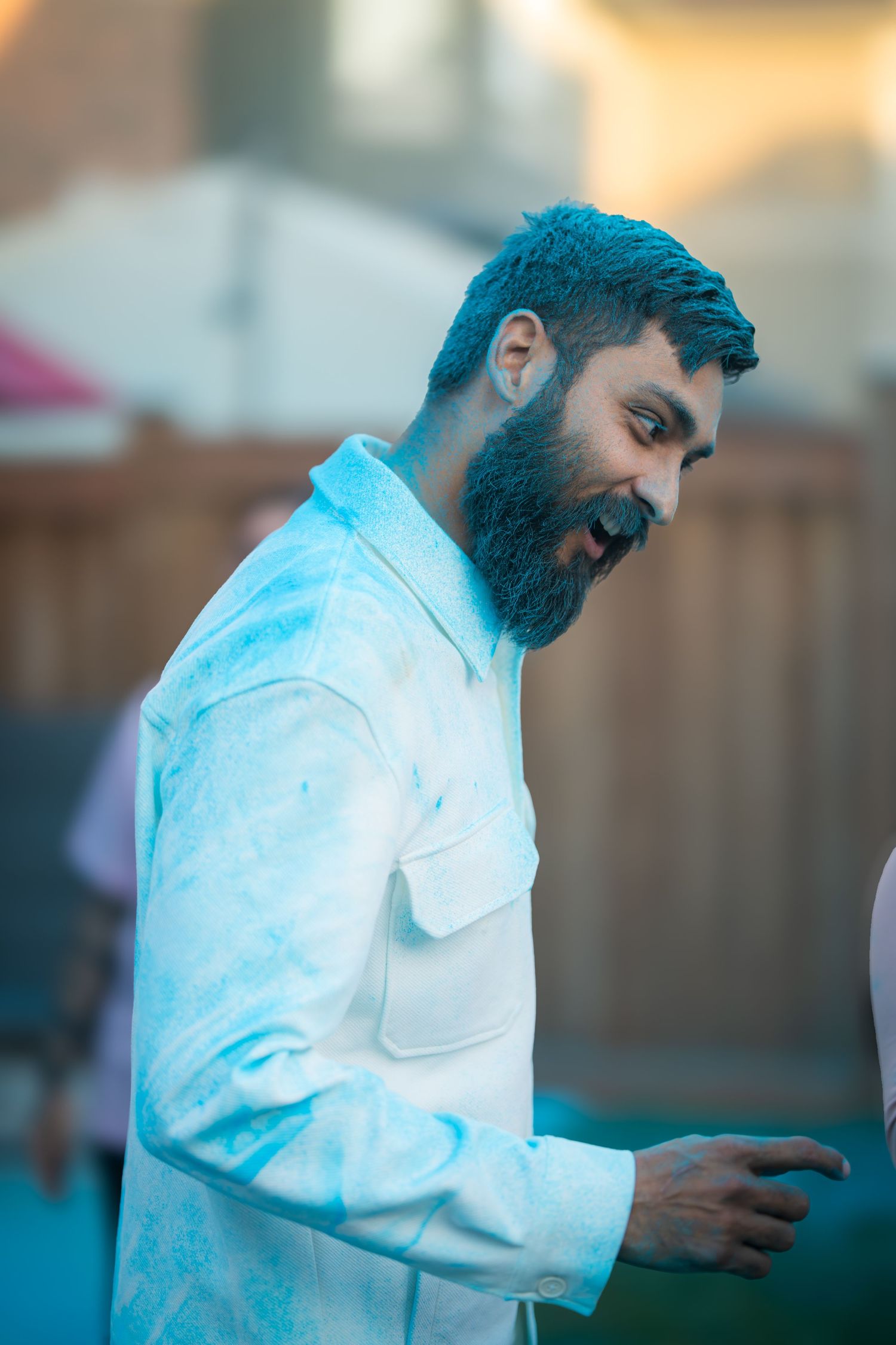 Bearded man in white jacket laughing outdoors at backyard celebration during golden hour.