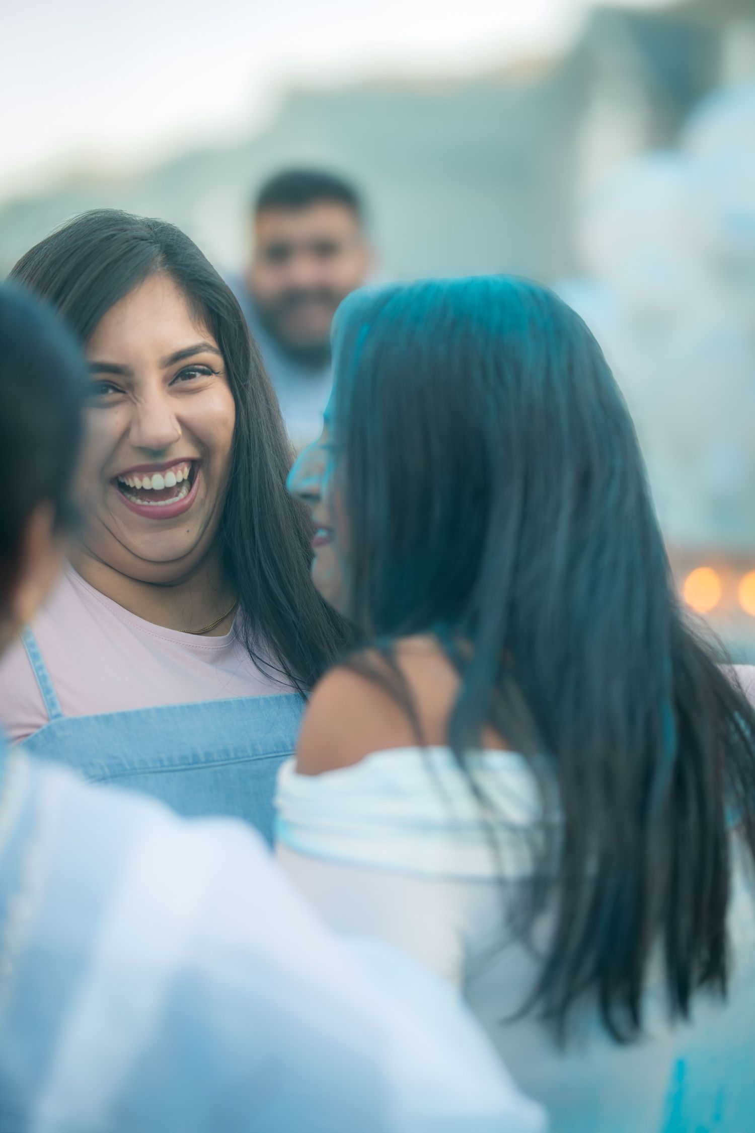 Two young women laughing and smiling together at an outdoor social gathering in the evening.