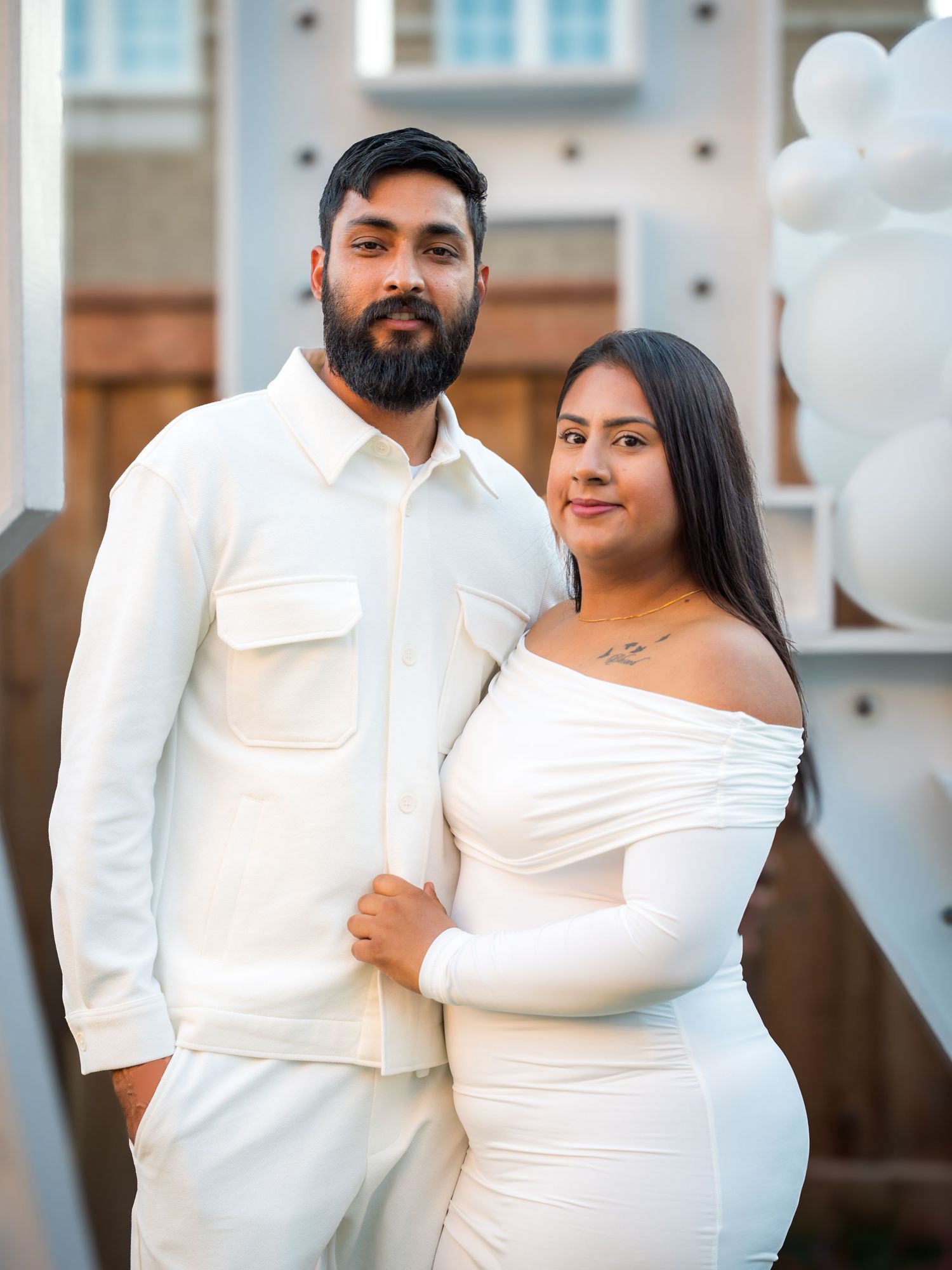 A couple dressed in coordinating white outfits poses together at an outdoor celebration event.